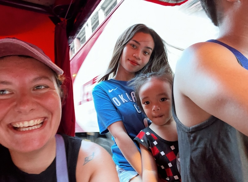 "Selfie aus dem Motorrad-Taxi. Sophia lächelt breit aus dem Beiwagen und am Motorrad sitzt der Fahrer samt Kind und Freundin."