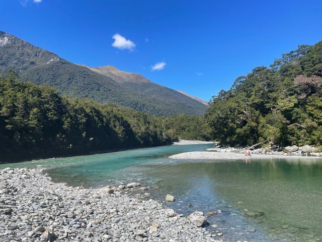 "Ein türkisfarbener Fluss, umgeben von weißen Steinen und grünen Wäldern."