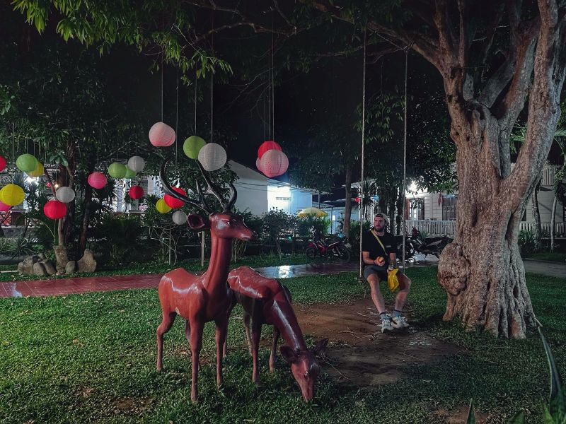 "An der Raststation sitze auf einer Schaukel neben einem Baum und zwei braunen Rehen aus Plastik. Am Baum hängen bunte Lampions"
