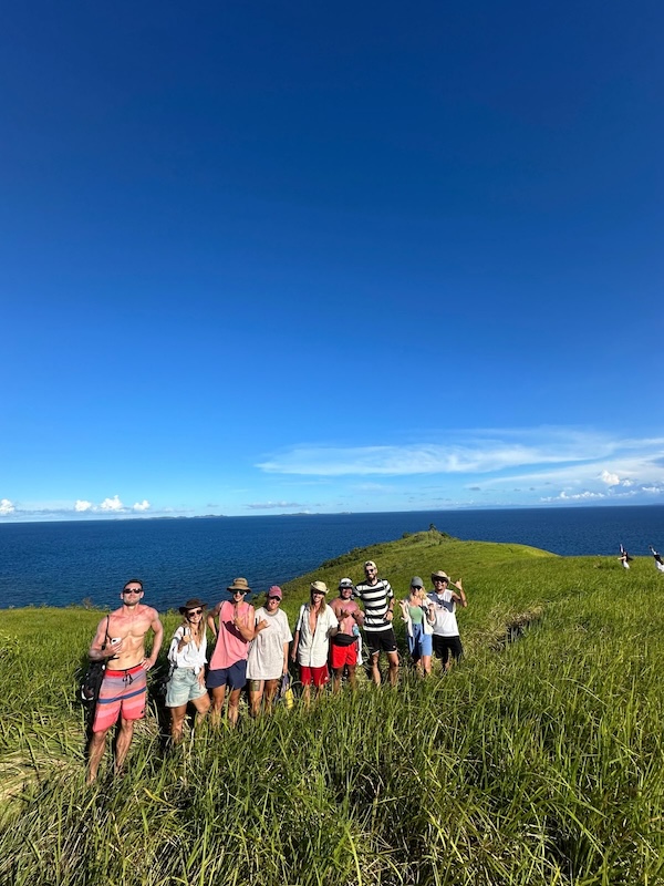 "Ein Gruppenfoto, von uns wie wir in einer Reihe vorm hohen Gras der Insel stehen."