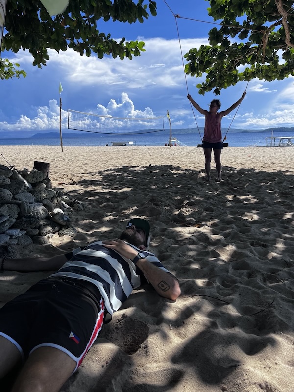 "Philippe sitzt auf einer Schaukel, die am Baum befestigt ist. Ich liebe am Sandstrand, im Schatten und halte meine Hand auf die Brust."