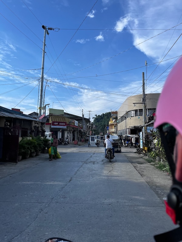 "Die Straße von Dapa. Vor mir fährt ein Moped und ein Tuktuk. Ein weiteres Tuktuk kommt mir entgegen."