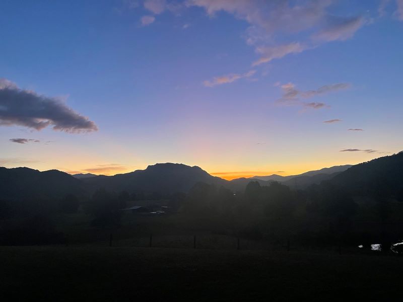 "Die Sonne geht hinter den Bergen von Murchison unter. Der Himmel ist blau und zeigt einen Übergang in Orange, wo die Berglandschaft beginnt."