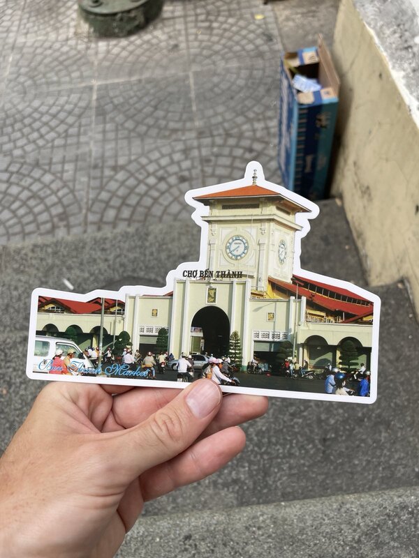 Ich halte eine Postkarte in meiner Hand: Das Saigon Central Post Office ist darauf zu sehen.