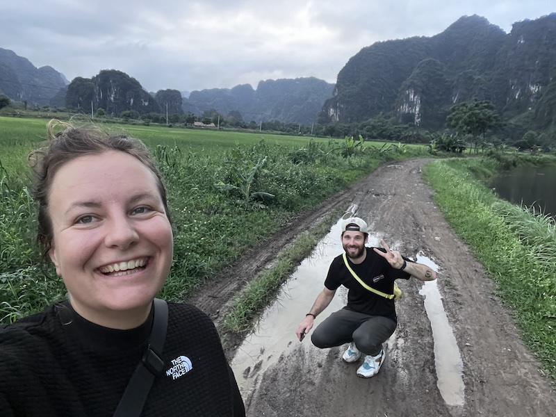 "Sophia und ich posieren auf einem matschigen Weg. Im Hintergrund erkennt man die grüne Landschaft Ninh Binhs."