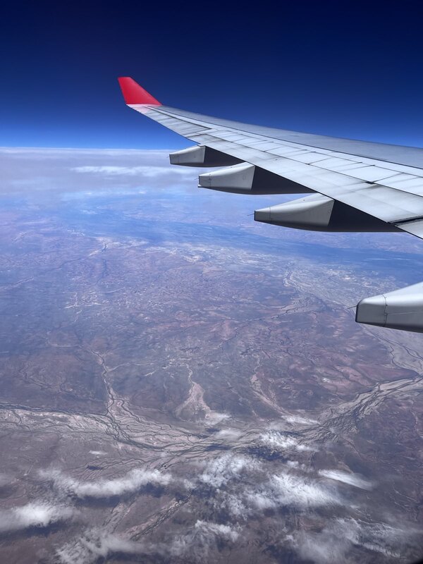 "Blick aus dem Flugzeug: unter einem dunkelblauen Himmel liegt ein großer Fluss, der die dunkelgraue Landschaft entzweiteilt."