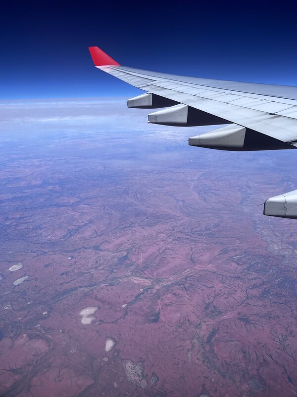 "Blick aus dem Flugzeug: unter einem dunkelblauen Himmel liegt eine rote Landschaft, durch die sich dunkle Landstriche ziehen."