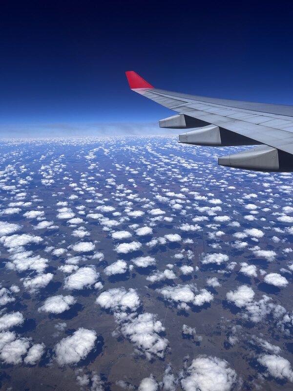 "Blick aus dem Flugzeug: unter einem dunkelblauen Himmel sammeln sich hunderte von kleinen Wölkchen, die sich über der Landschaft sammeln."