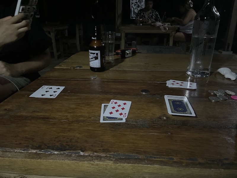 "Spielkarten und eine Bierflasche stehen auf dem verdunkelten Holztisch"