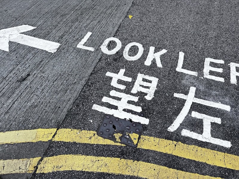 "Eine Straßenmarkierung am Straßenrand, auf der Look Left und die chinesische Übersetzung steht"