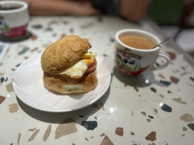 "Auf dem Tisch steht ein Teller mit einem weichen Sandwich, gefüllt mit Ei und Tomaten. Daneben steht ein Milchtee."