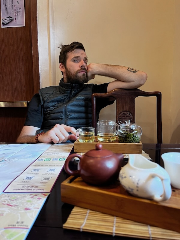 "Ich sitze entspannt am Stuhl und stütze meinen Kopf an meiner Hand ab. Vor mir steht ein Tee."