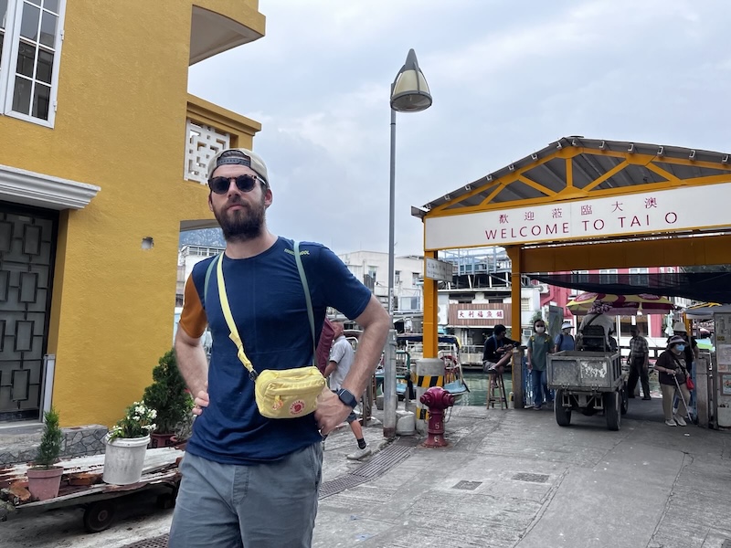 "Ich stehe vor einem Bogen auf dem "Welcome to Tai O" steht."