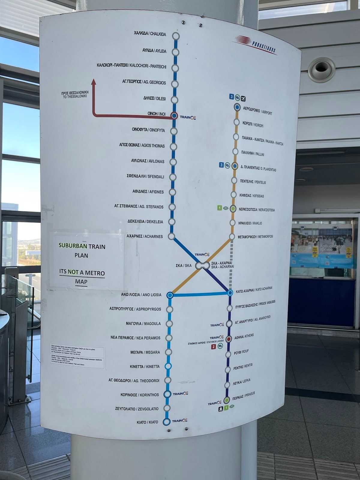 Eine grafische Darstellung der Athener Zugverbindungen. 4 Linien in je unterschiedlicher Farbe zeigt das Verkehrsnetz. Am linken Rad klebt ein weißes Papierblatt auf dem folgenden Text in Großbuchstaben steht: "Suburban Train Plan. It's Not a Metro Map"