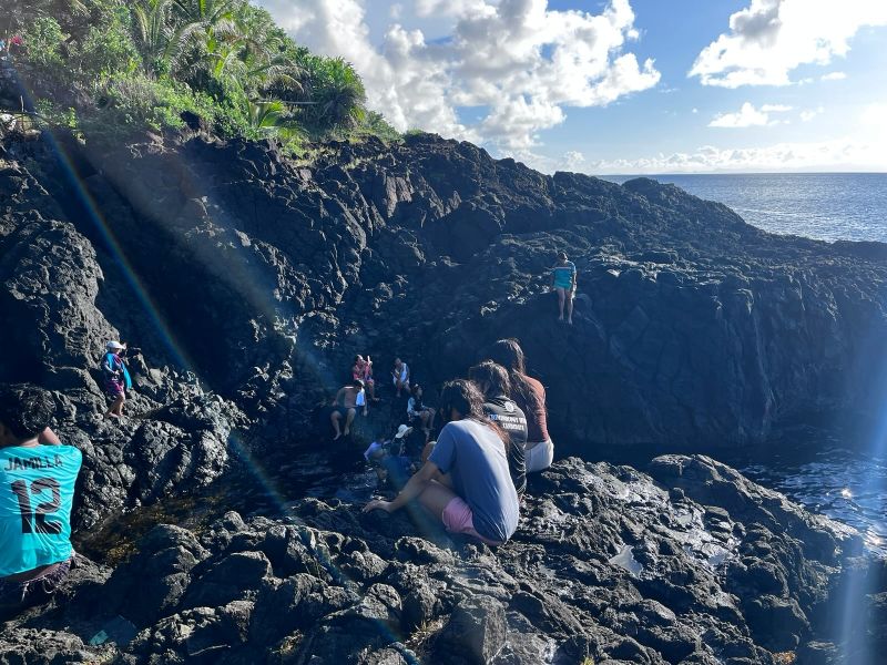 "Einige schroffen Felsen auf rund ein dutzend junge Filipinas und Filipinos sitzen. Die Sonne strahlt."