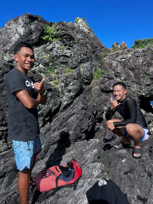 "Chad mit erhobenen Daumen und Jan-Jan mit dem Surfergruß auf den Felsen"