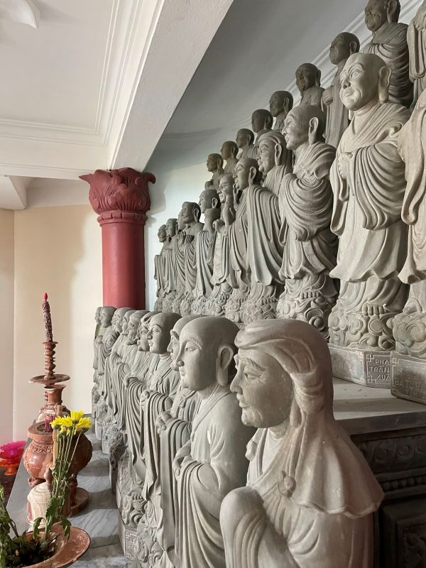 "Eine Vielzahl von grauen Steinfiguren, die gerade aus sehen und ihre Hände unter der Robe gefalten haben. Alle haben unterschiedliche Gesichtsformen."
