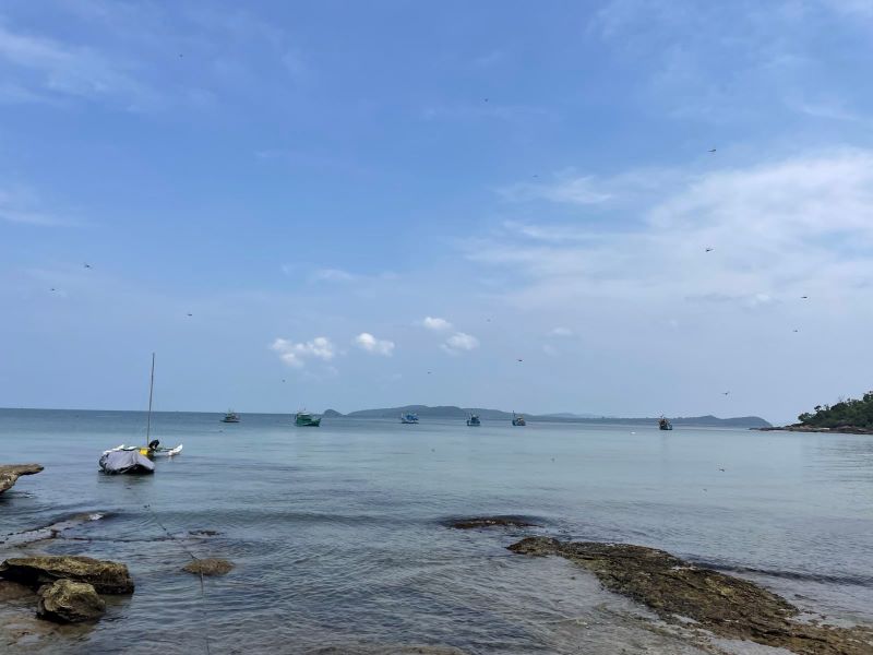 "Am Meer sind ein paar Fischerboote zu erkennen. In der Ferne liegt eine Insel, die sich über den Horizont erstreckt."