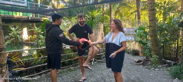 "Der Mopedverleiher überreicht Sophia einen orangen Helm. Ich stehe dazwischen und kratze mein Bein."