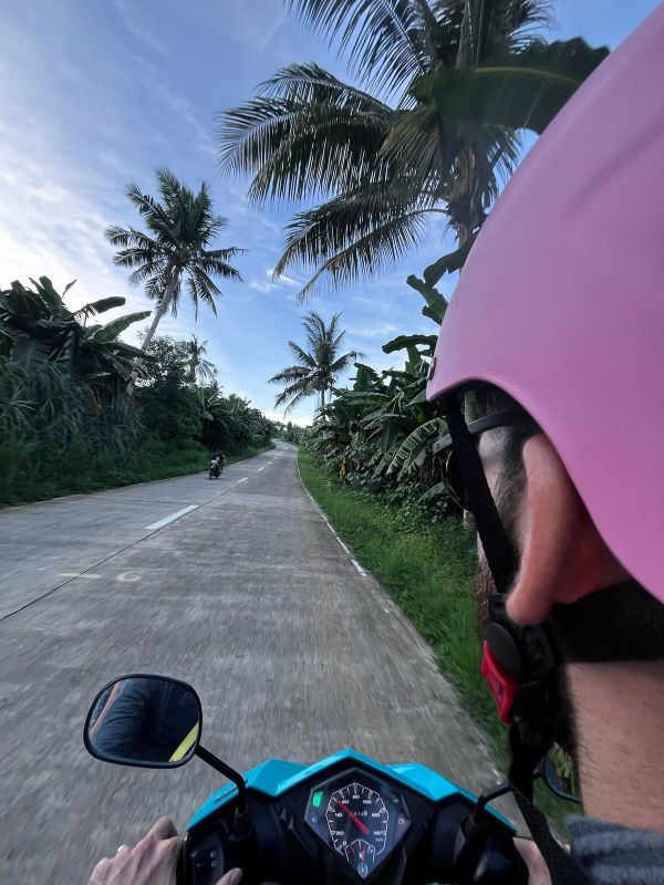 "Blick über meine Schulter wie ich Moped fahre. Die Straße ist frei, mir kommt ein anderes Moped entgegen."