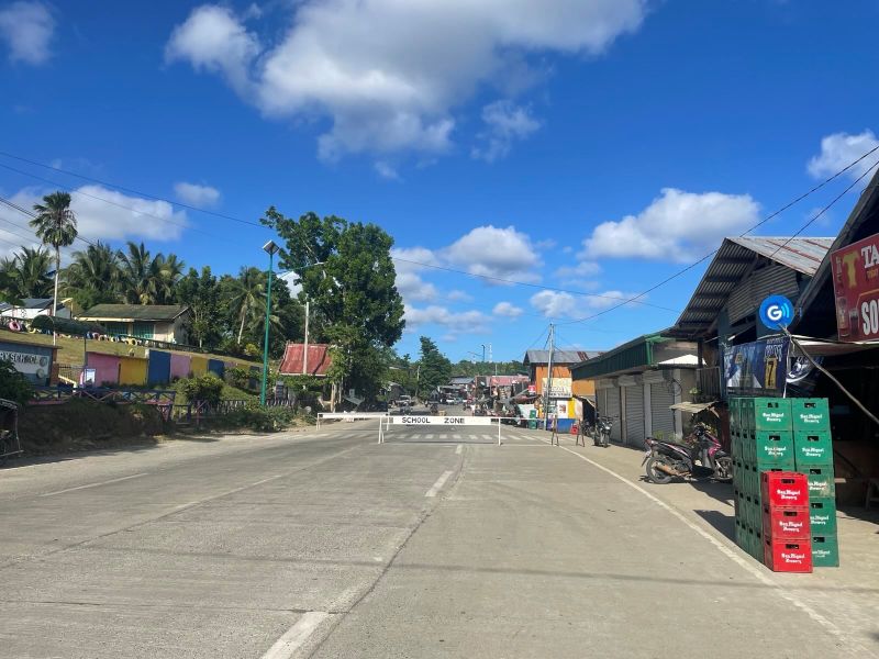 "Ein ruhiges Dorf, in dem auf der Fahrbahn ein Schild den Weg versperrt: Darauf steht: School Zone."