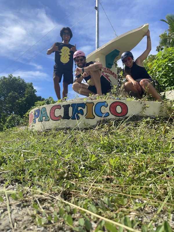 "David, Sophia und ich posieren vorm Ortseingang von Pacifico: einem steinernen Surfbrett auf einer Platform auf der "Welcome to Barangay Pacifico" steht."