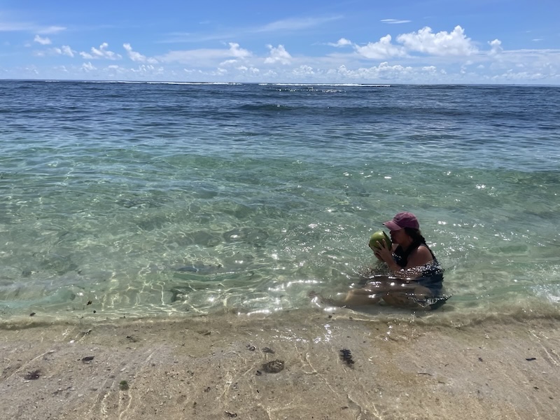 "Sophia schwimmt im blau-türkisen Meer von Pacifico. Sie trägt eine rote Kappe und schlürft aus ihrer grünen Kokosnuss."