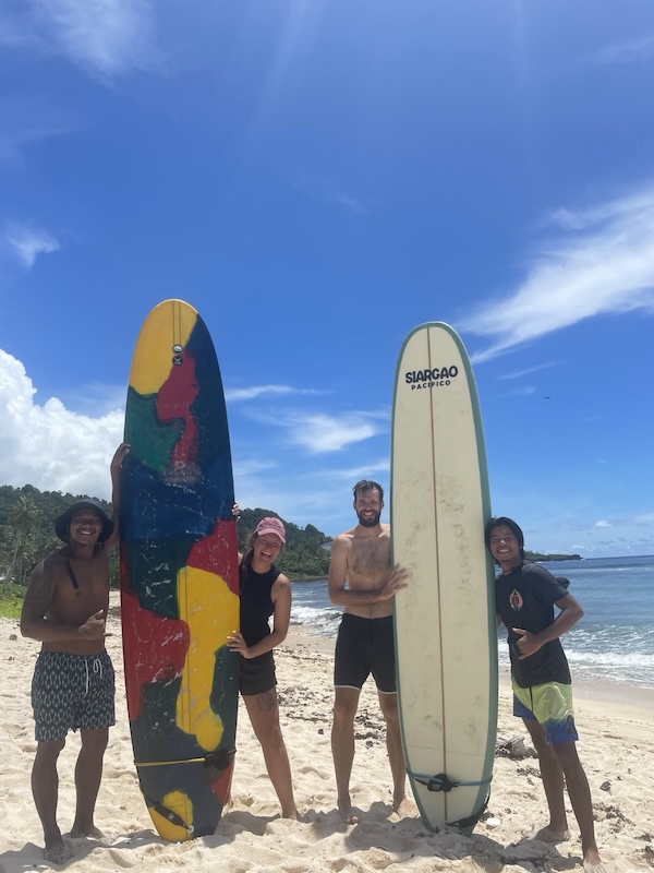 "Wir vier stehen am Strand und posieren neben unseren Surfbrettern, die wir senkrecht aufgestellt haben. Sophia mit ihrem Lehrer Ambum und ich mit David."