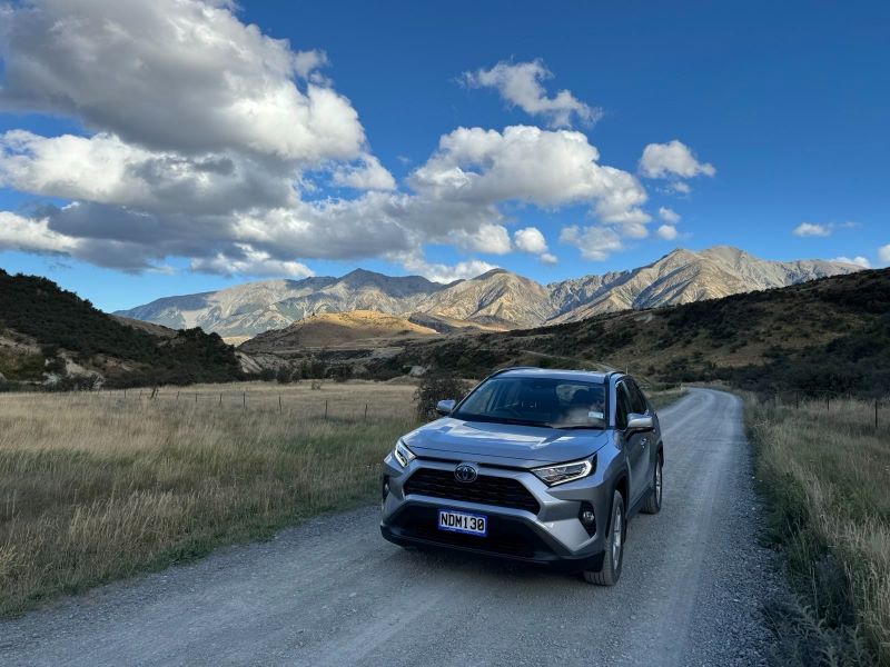 "Ein Auto parkt auf einem Schotterweg mit Bergen und einem blauen Himmel mit Wolken im Hintergrund"