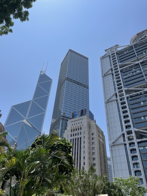 "Drei Gebäude stehen am Statue Square: ein scharfes kantiges ganz links, der Bank of China Tower, das Cheung Kong Center und das HSBC Gebäude mit Kanonen auf dessen Dach, ganz rechts."