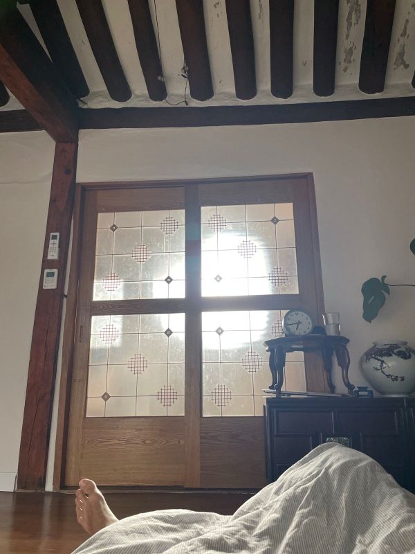 "Der Blick aus dem Bett, das am Boden ist auf die durchsichtige Schiebetür, durch die das morgendliche Licht durchdringt."