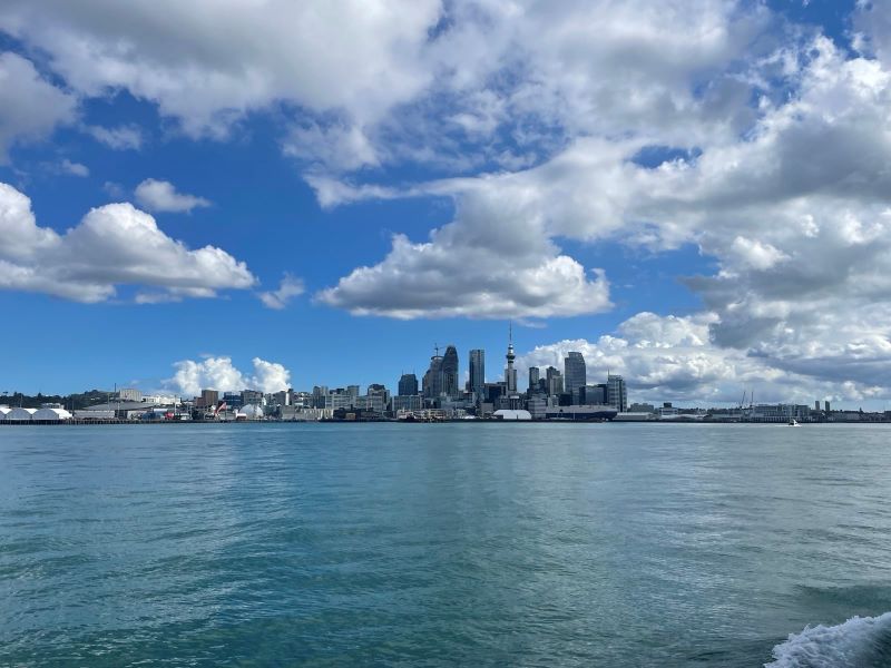 "Die Skyline Aucklands vom Wasser aus. Ein Einige Wolken sind über den großen Gebäuden zu sehen."