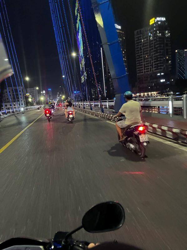 "Auf der Brücke fahren einige Mopeds vor mir. Die Brücke leuchtet in blauer Farbe."
