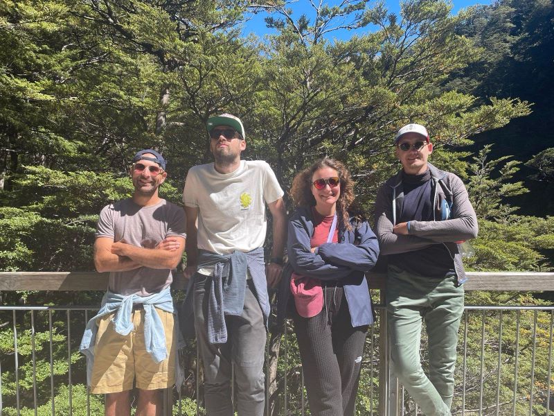 "Unser Gruppe wie sie vor einem grünen Wald steht. Alle lächeln in die Kamera, nur ich schaue wo anders hin. Alle sind sportlich gekleidet."