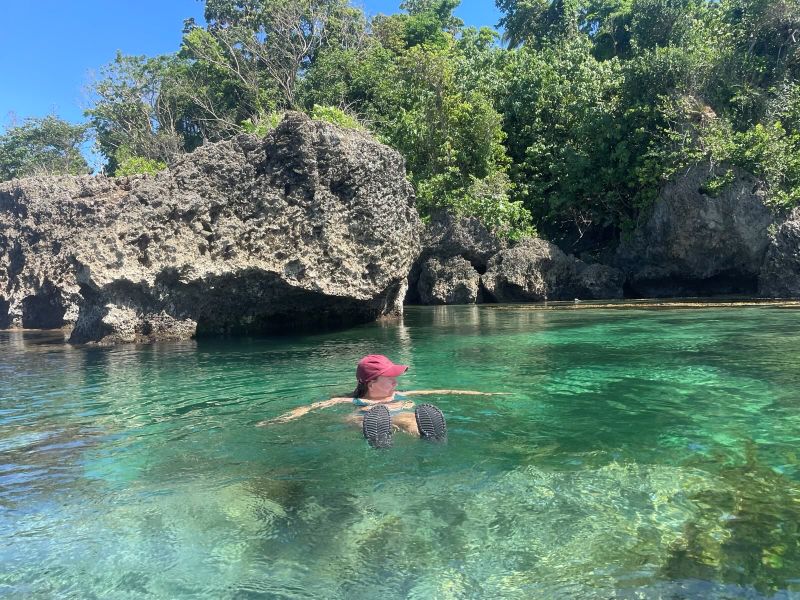 "Sophia wie sie im Felsbecken schwimmt. Sie trägt ihre rote Kappe und blickt zur Seite."