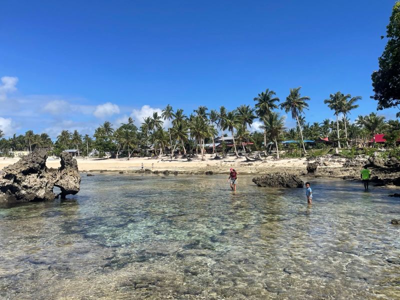 "Vom Strand aus spaziert Sophia am Wasser entlang. Vereinzelt stehen einige Felsen aus dem Wasser. Auch der Boden ist besteht aus schroffen Felsen."