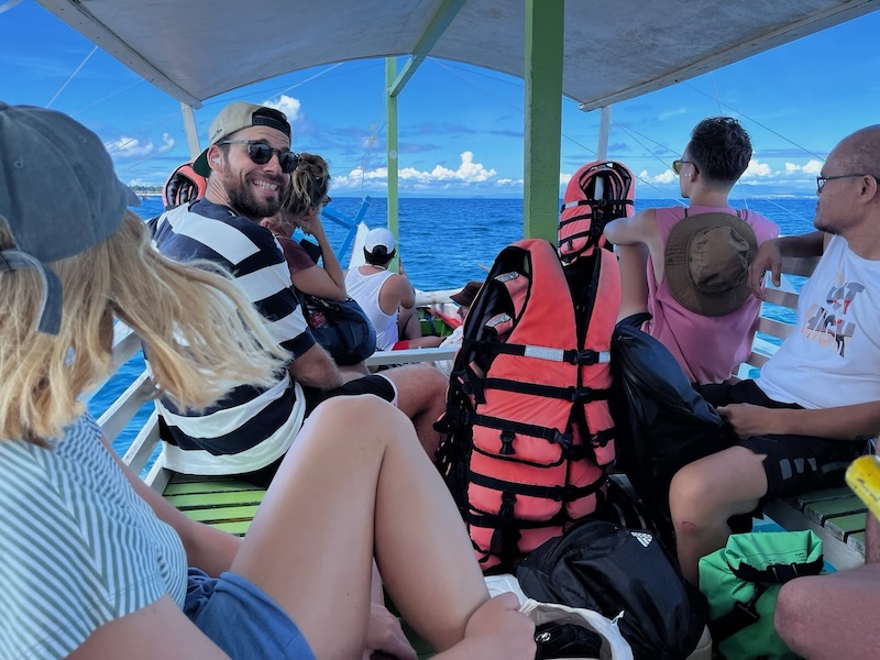 "Der Bug des Bootes, vorne sitzen die andere Sophia, Jennifer, Miguel, Philippe, Wesson und ich. Ich grinse in die Kamera, alle anderen schauen gerade aus ins Blau des Ozeans."