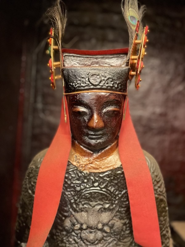"Eine der Statuen im Tempel ist eine Figur mit braunem gesicht und einer rituellen Bekleidung und einem auffallenden Hut mit Federn und roten Bändern."