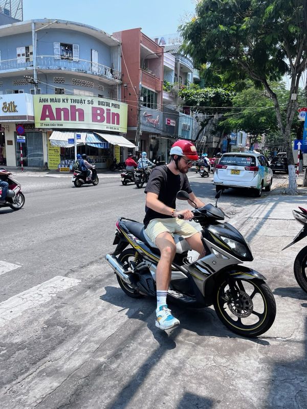 "Ich sitze auf Mopi und biege auf einen Parkplatz ein. Hinter mir Fahren eine Mopeds über die Kreuzung."