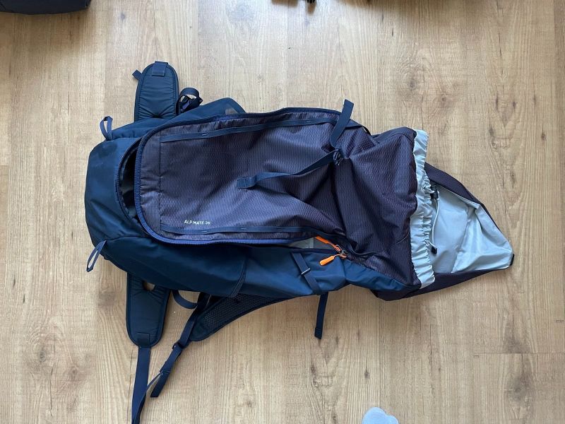 Ein blauer Rucksack liegt mit geöffnetem Reißverschluss auf dem Parkettboten. Der obere Teil des Rucksacks ist ebenfalls geöffnet.