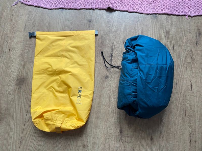 Auf dem Parkettboden liegt ein gelbes Drybag neben einer blauen, zusammengerollten Jacke