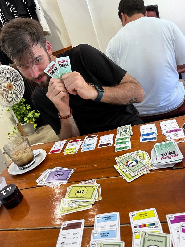 "Ich verstecke mich hinter zwei Spielkarten von Monopoly Deal. Am Tisch sind noch mehr Spielkarten aufgelegt."