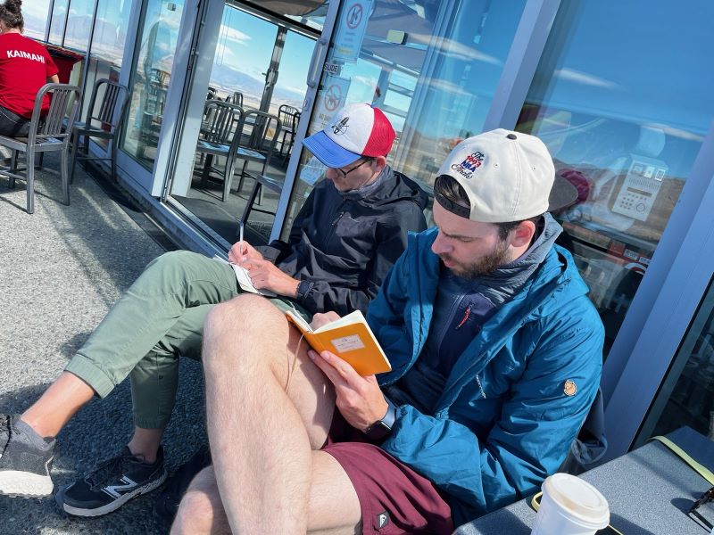 "Manu und ich sitzen auf einer Terrasse in der Sonne und sind beide sehr fokussiert wie wir jeweils in unsere Notizbücher schreiben."