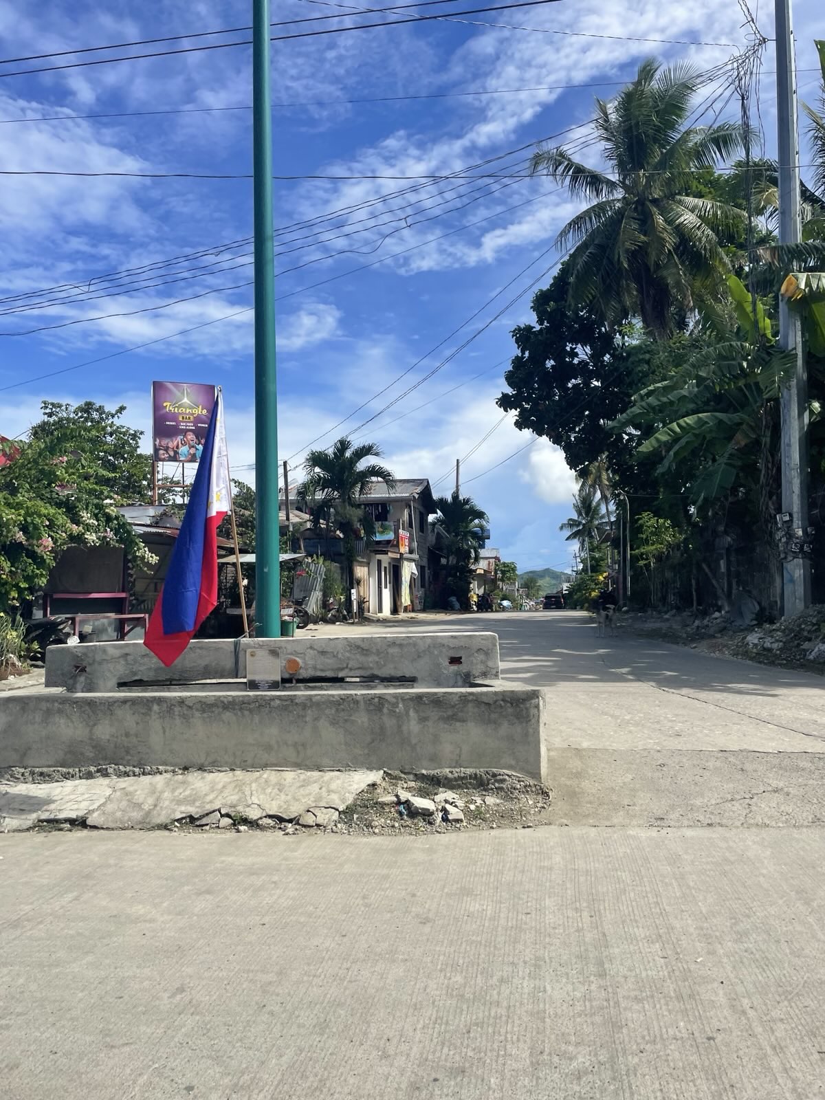 "Am Boden eines Fahnenmastes steckt die philippinische Flagge. Dahinter verläuft eine Straße unter einem blauen Himmel."