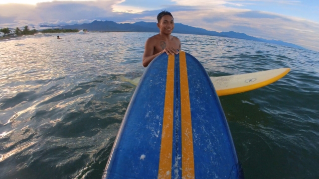 "Chad am Meer, auf seinem gelben Surfbrett wie er lächelt und seine Hand auf die Spitze meines Surfbretts legt."