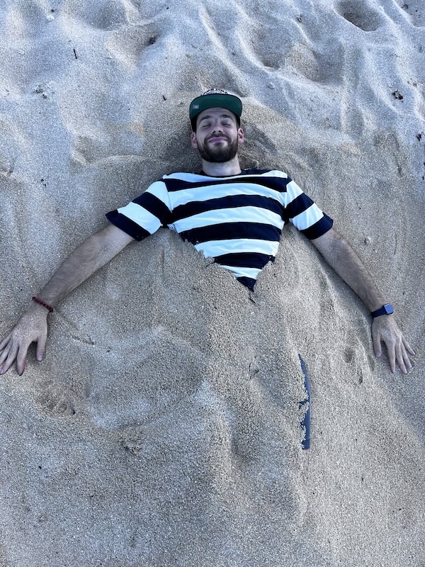 "Ich bin mit dem Unterkörper im Sand eingegraben und strecke meine Hände zur Seite aus. Ich habe mein blau-weiß gestreiftes T-Shirt an und meine Kappe auf. Ein zufriedenes Lächeln zeichnet sich auf meinem Gesicht ab."