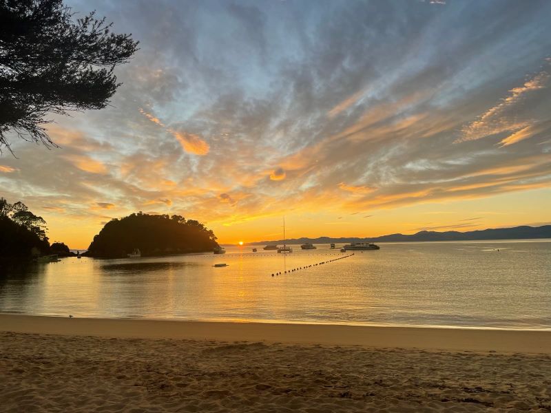 "Die aufgehende Sonne am Horizont wirft ein oranges Licht auf das Meer. Über dem Meer ist ein bewölkter Himmel zu sehen."