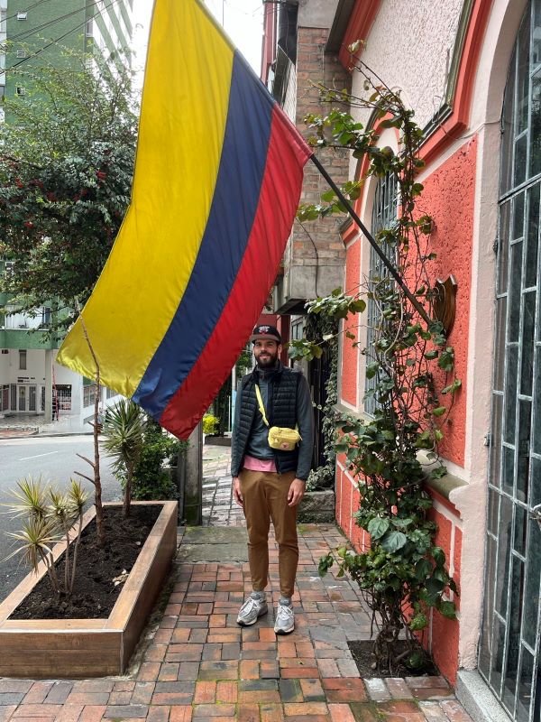 Ich stehe auf einer Straße neben einem Haus mit rot-weißer Fassade. Über mir weht eine große kolumbianische Flagge.